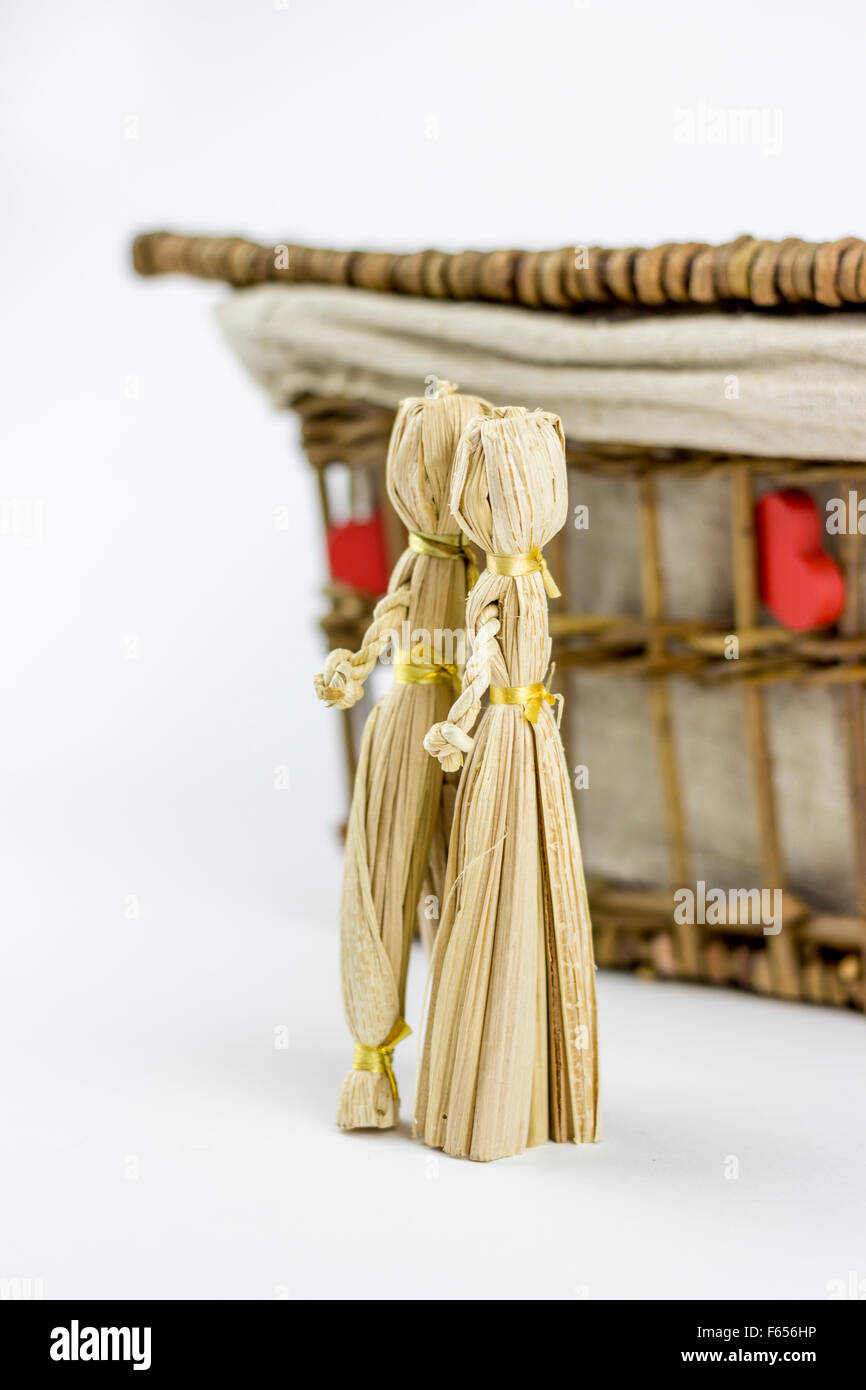 Two straw dolls kissing in front of an old rattan box, on a white
