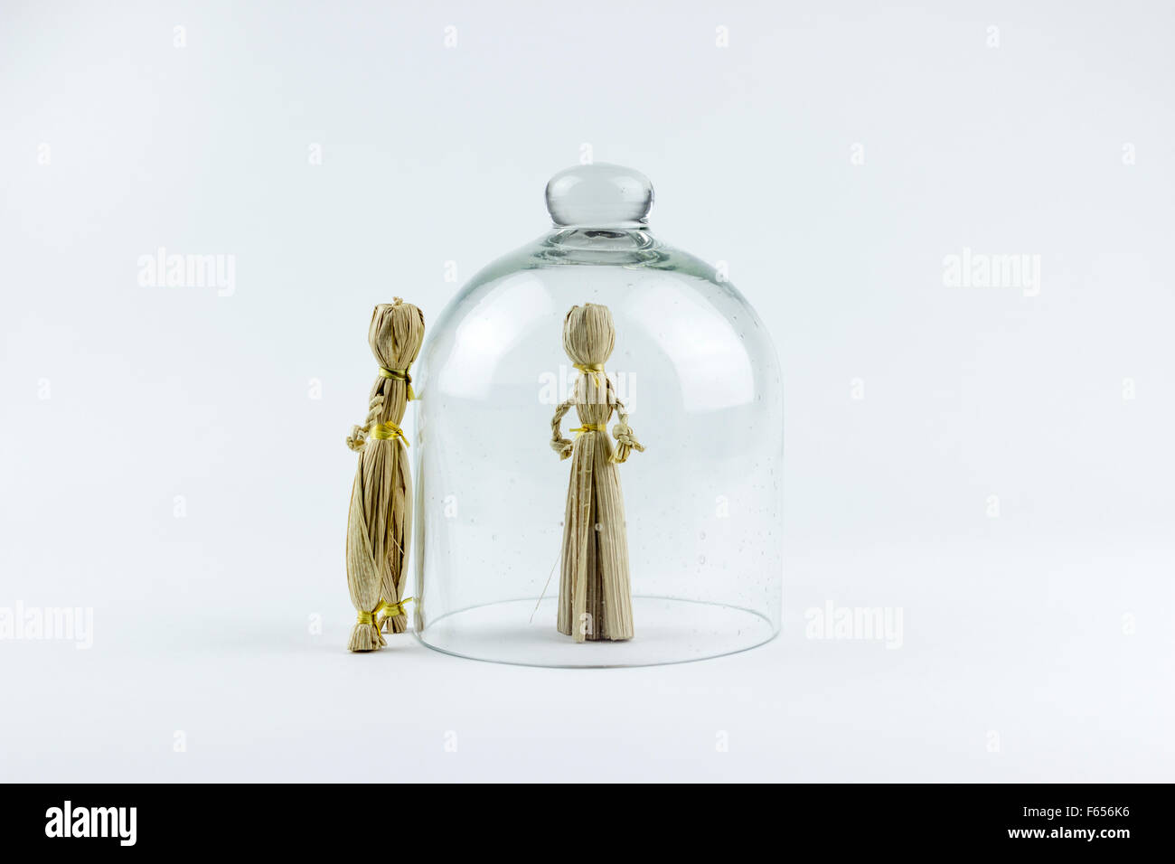 Man and woman straw dolls, divided by a glass bell, on a white background Stock Photo