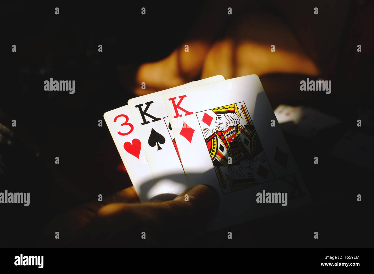A hand holds three playing cards during a card game. Stock Photo