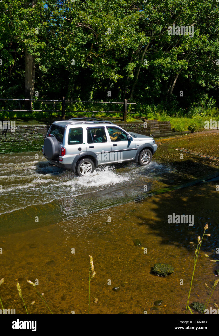 Car driving through a water filled ford crossing a stream on a country lane in England UK Stock Photo