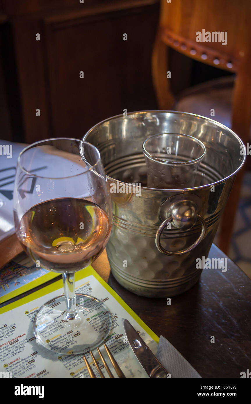 A glass of rosé wine and its carafe in a shiny ice bucket on a restaurant table, Bergues, Nord Pas de Calais, France Stock Photo