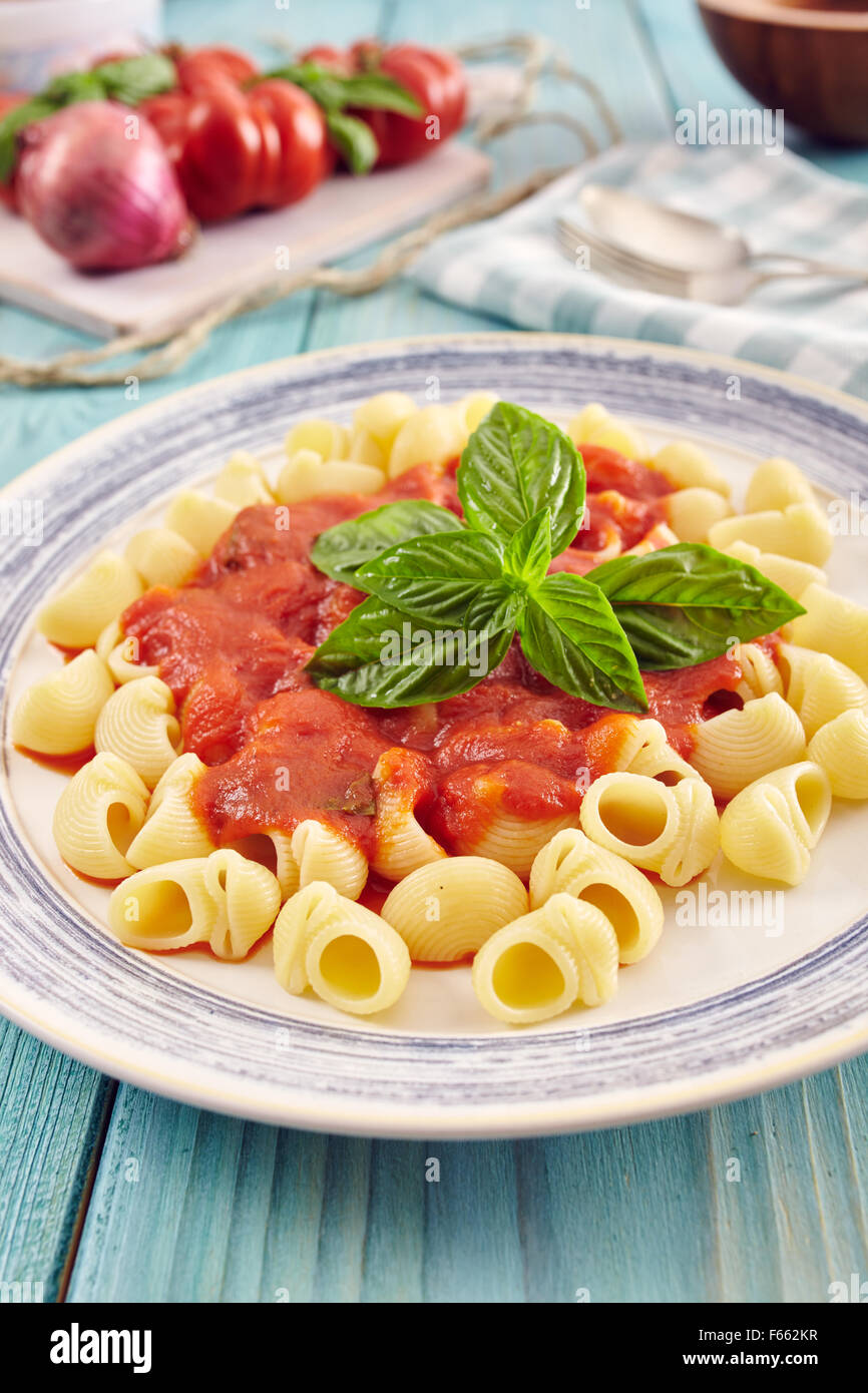 pasta conchiglie type with tomato sauce on an aquamarine wooden table surrounded by fresh tomatoes and onion Stock Photo