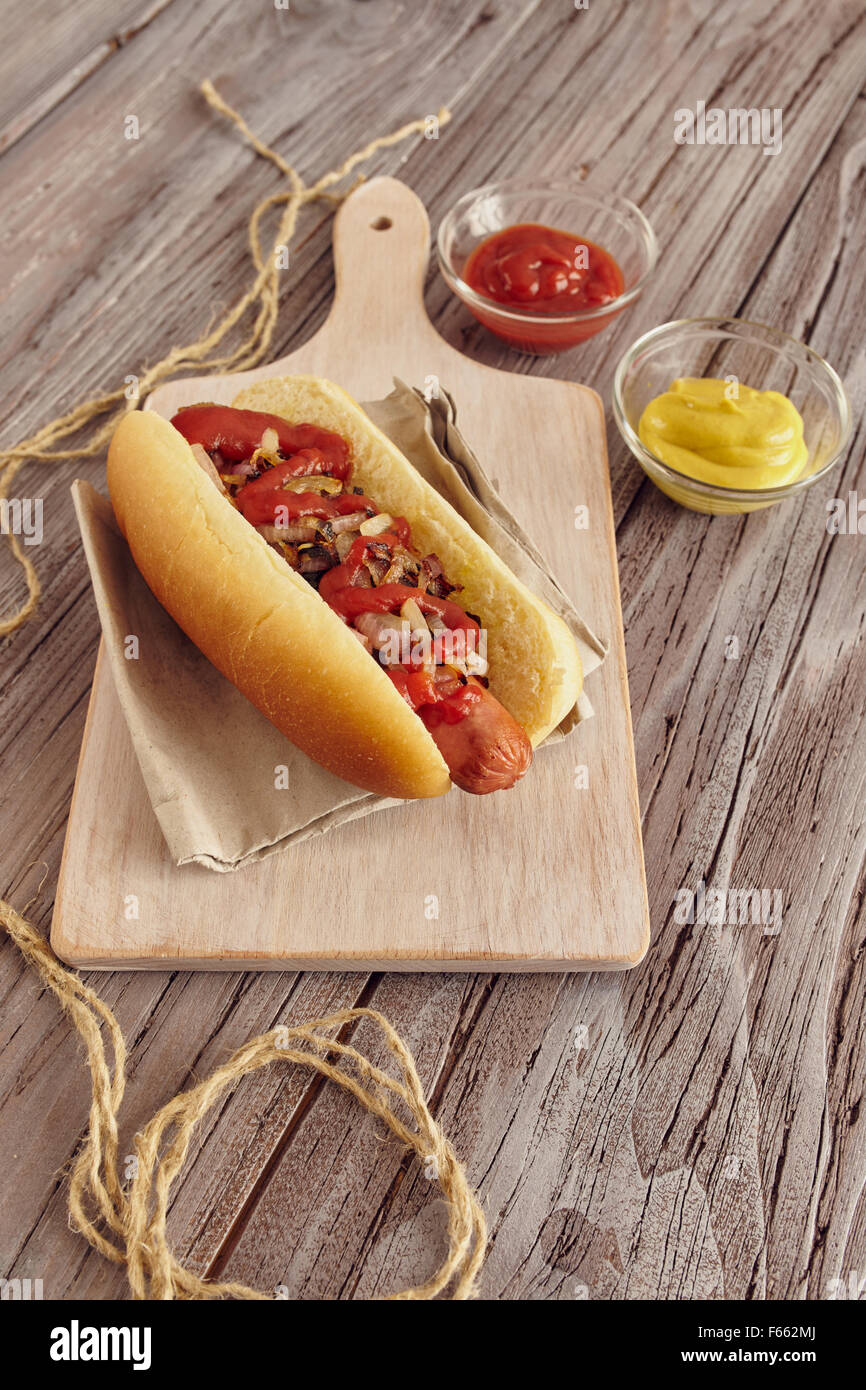 Hot dog with onion, ketchup and mustard on a white chopping board on a