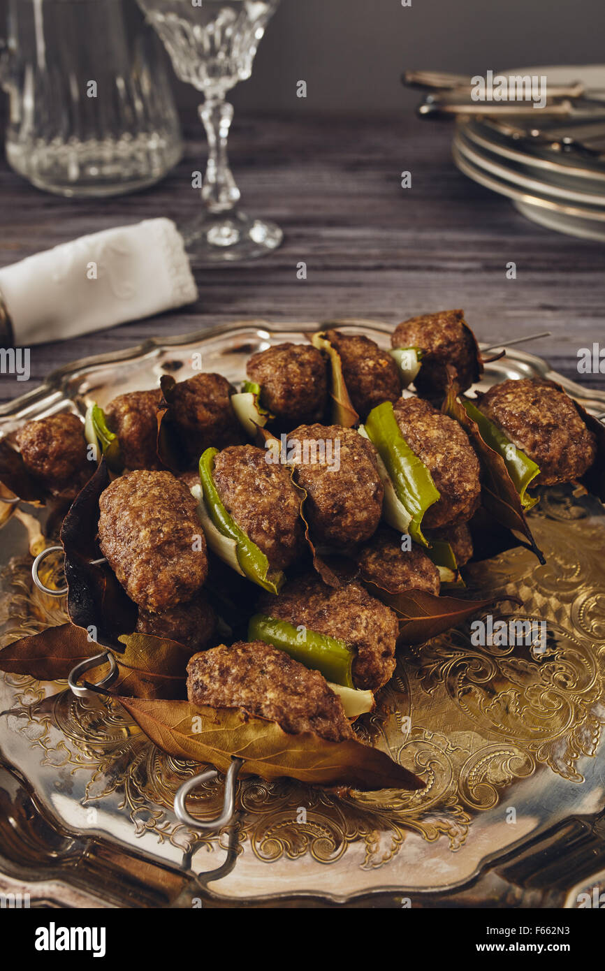 mince meatball on a spit (Italian dish) surrounded by glass, dishes and cuttlery, an elegant napkin on the table. everything on  Stock Photo