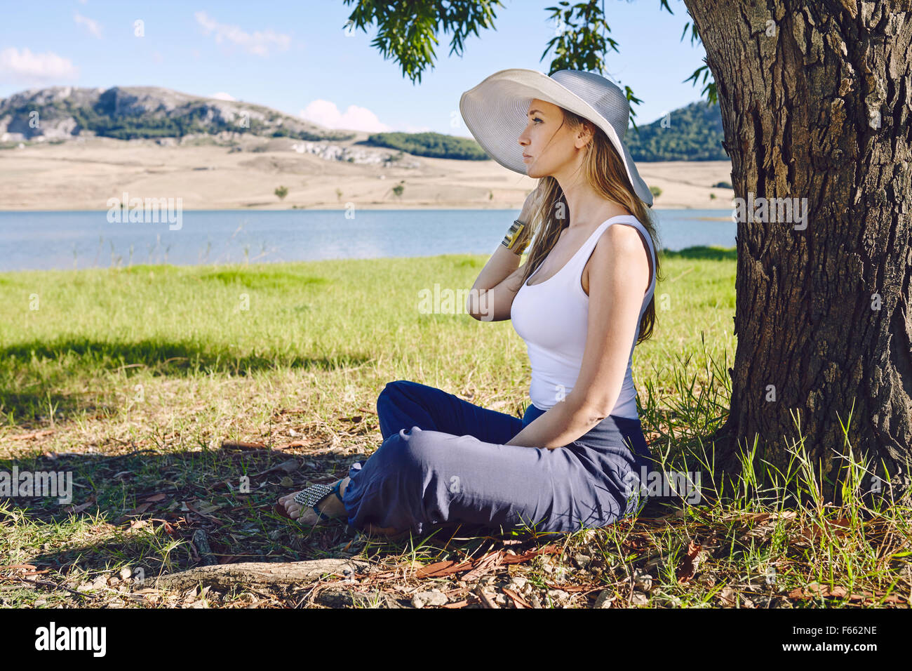 Blonde woman under a tree with a white hat Stock Photo