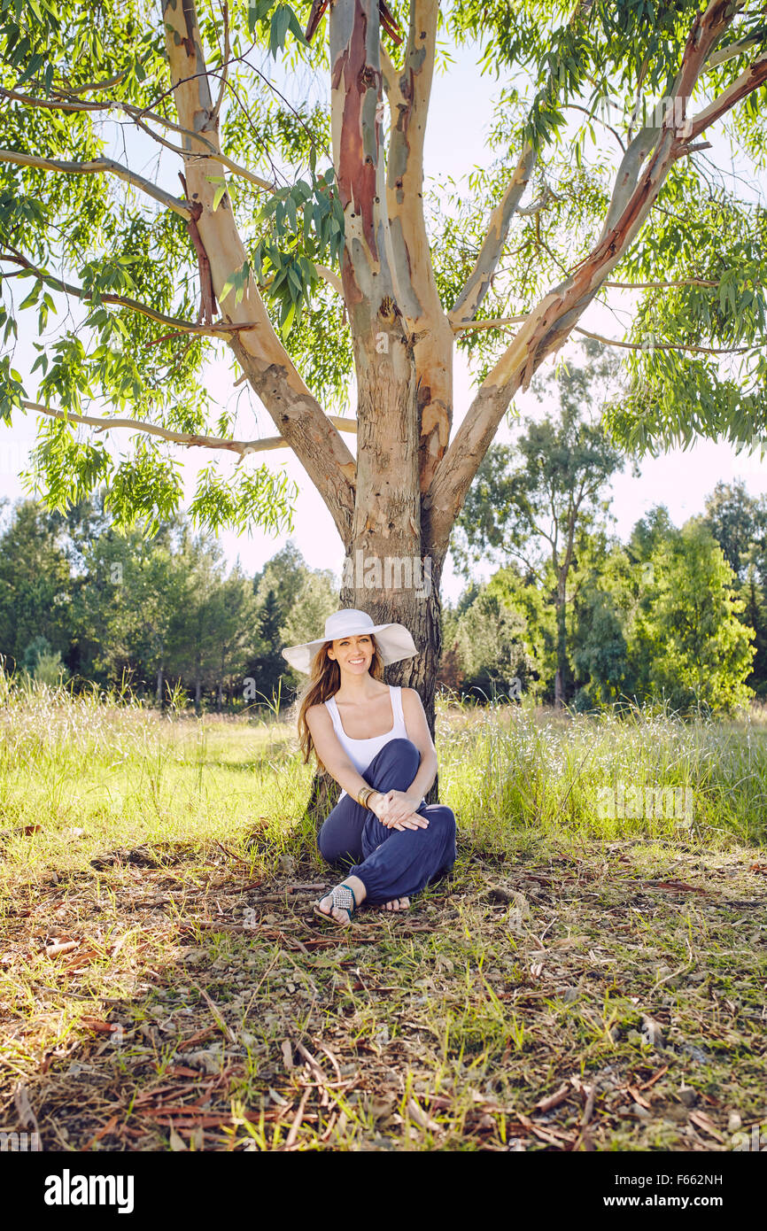 Blonde woman under a tree with a white hat Stock Photo