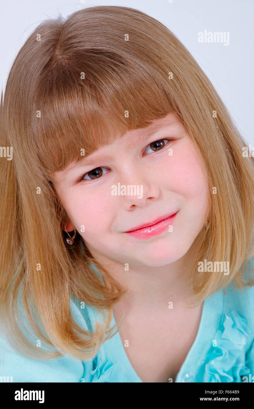 Portrait of a blond haired young girl looking directly at the camera on a white backdrop wearing a green shirt. Stock Photo