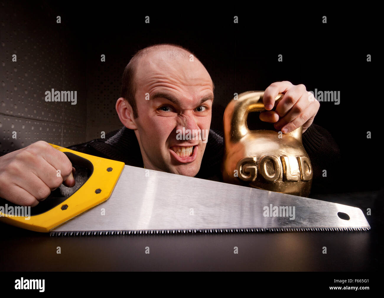 Crazy man with saw and heavy weight of gold Stock Photo