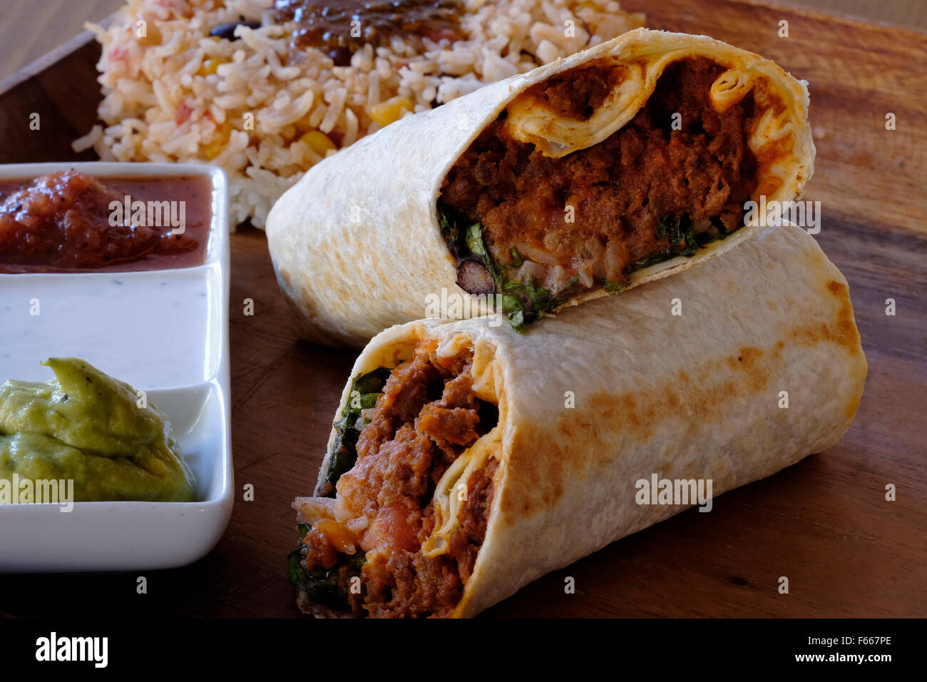 Beef burritos rolled in flour Tortilla with black bean spread served with Mexican rice and a side of salsa, guacamole and sour c Stock Photo