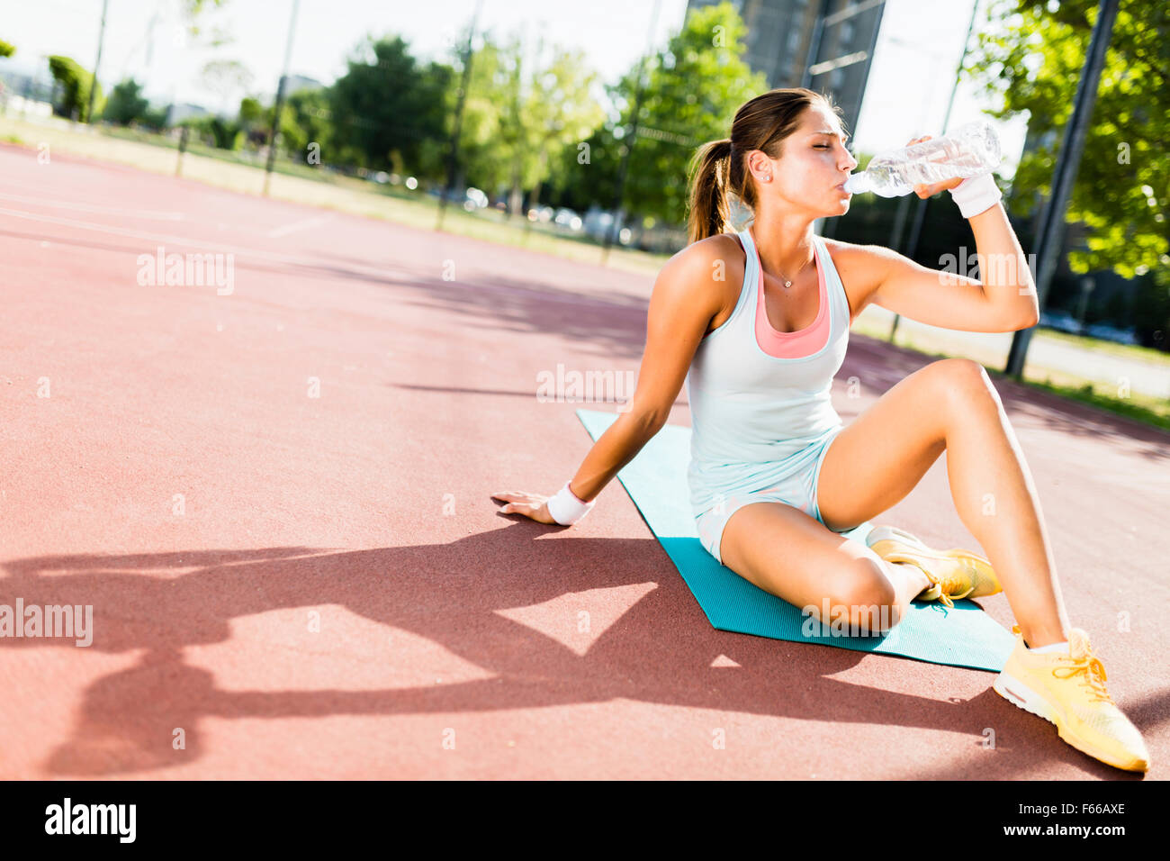 Young beautiful woman drinking water after exercise in a city training court on a sunny day Stock Photo