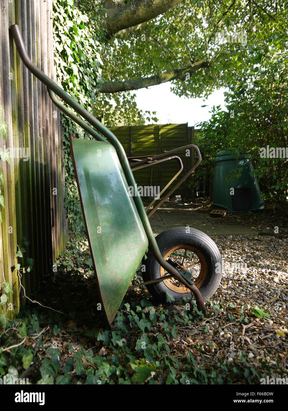 Green Wheelbarrow propped against wooden fence Stock Photo