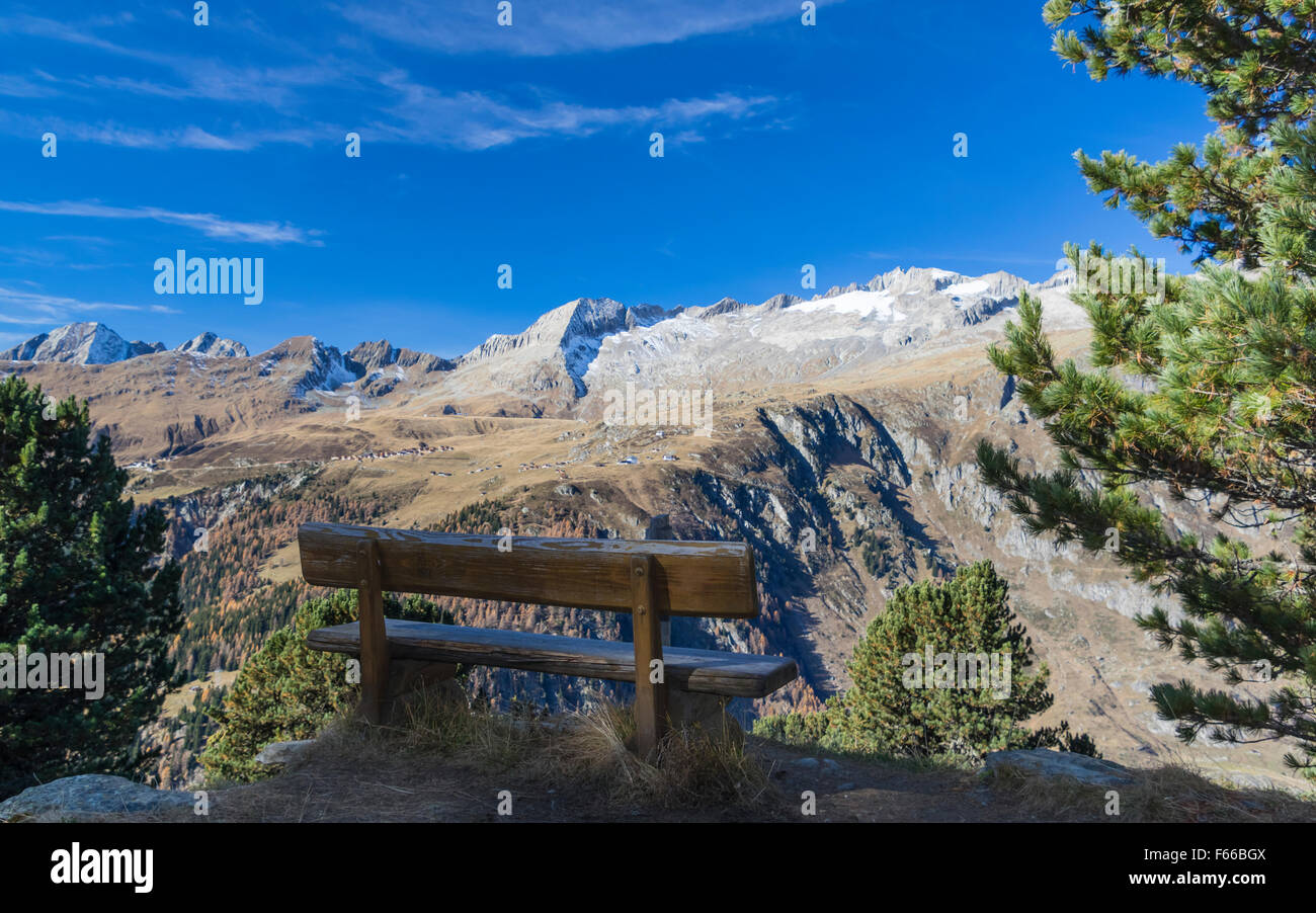 A bench in an Alpine region of Valais, Switzerland, with a splendid view of the settlement of Belalp and the mountains. Stock Photo