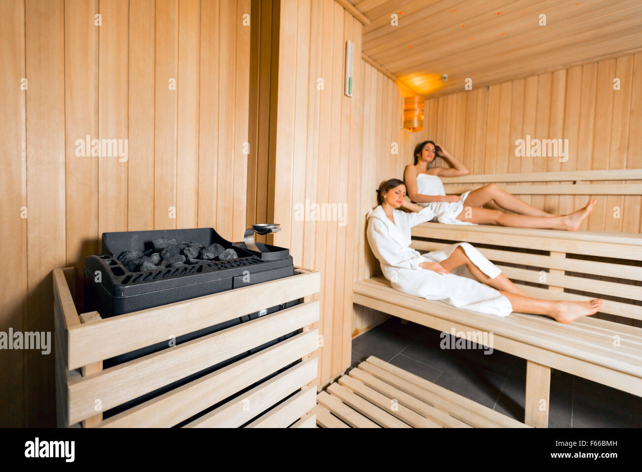 Sauna heater in a cozy sauna and girls relaxing in the background Stock Photo