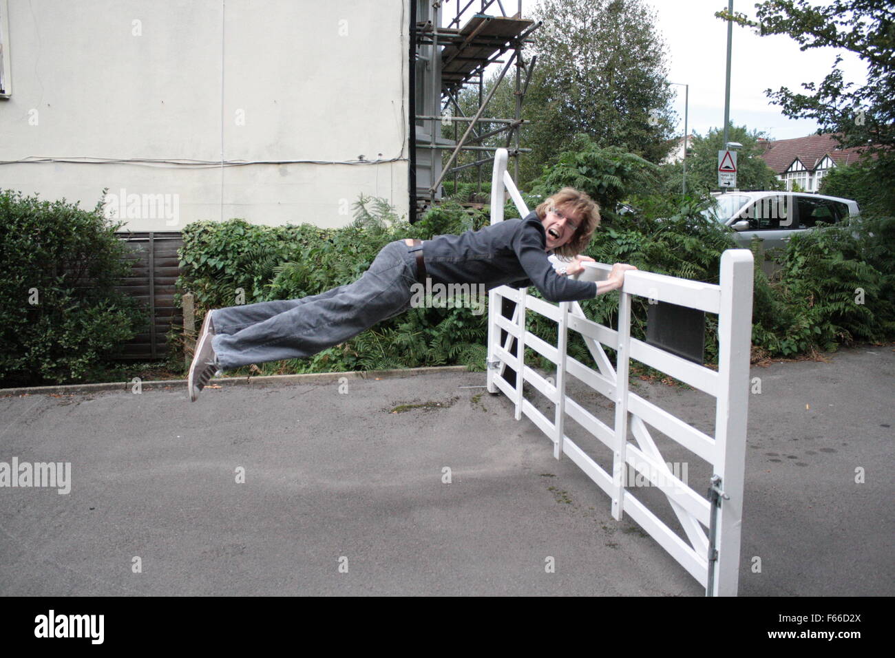 Man being blown away by a strong wind holding on to a gate (levitation) Stock Photo