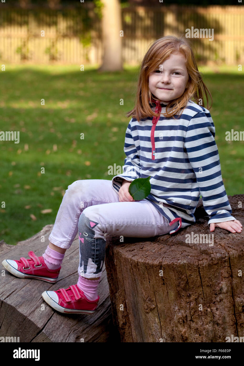 A young girl with ginger hair sits in the shade of the late afternoon autumn day. Stock Photo