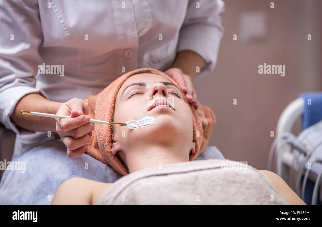 Young woman in spa salon, beautician applying facial mask to her Stock Photo