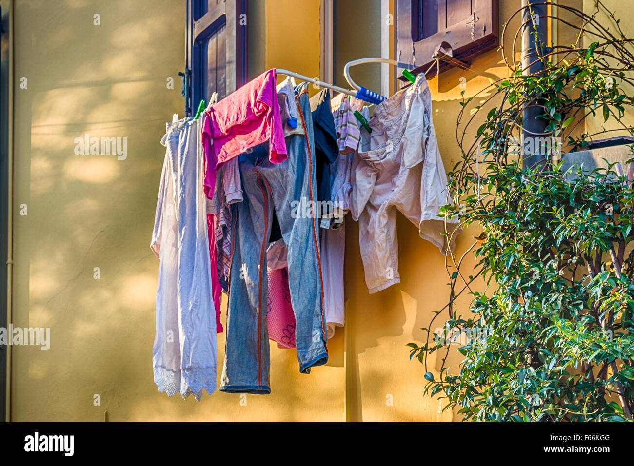 washed clothes hung out to dry on a drying rack hanging from a window in a house in Italy Stock Photo