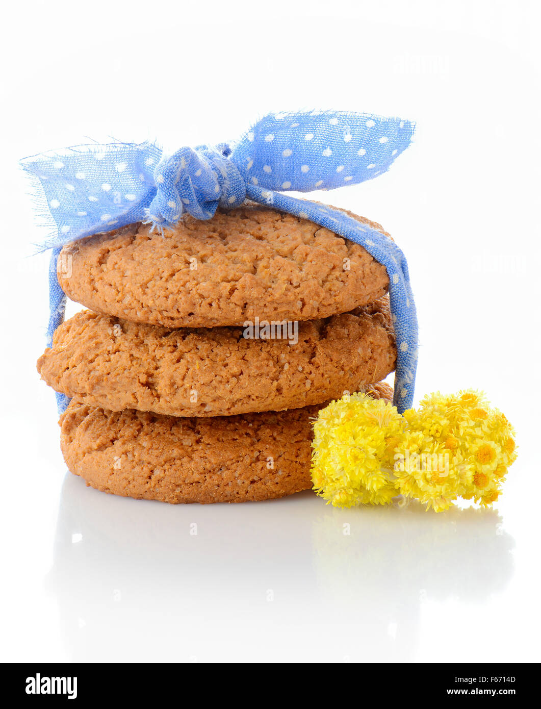 Stack of three homemade oatmeal cookies tied with blue ribbon in small white polka dots and tiny yellow flowers, isolated Stock Photo