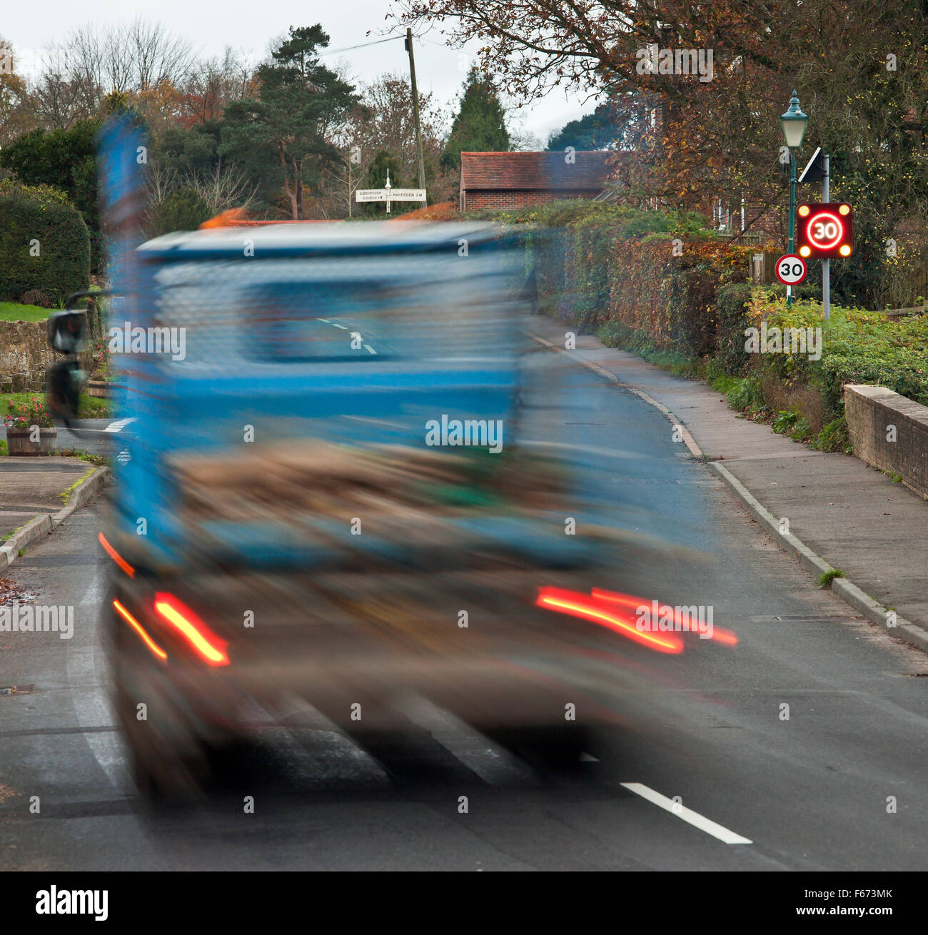 Speeding truck passing through a rural village, with the over 30mph warning sign flashing. Stock Photo