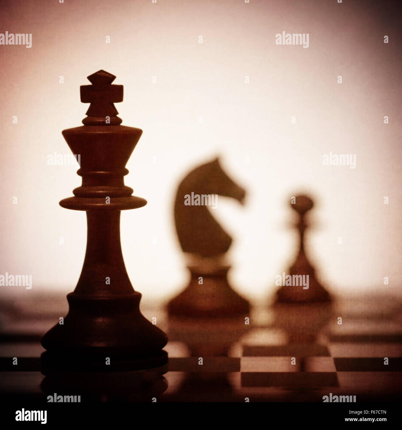 A close up of the King chess piece in silhouette with two other pieces in the background Stock Photo