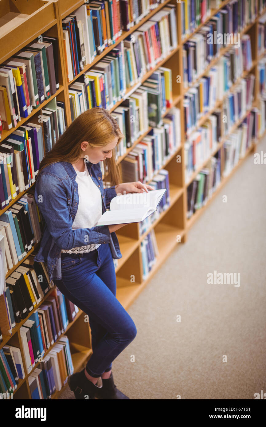 Student reading book in library leaning against bookshelves Stock Photo