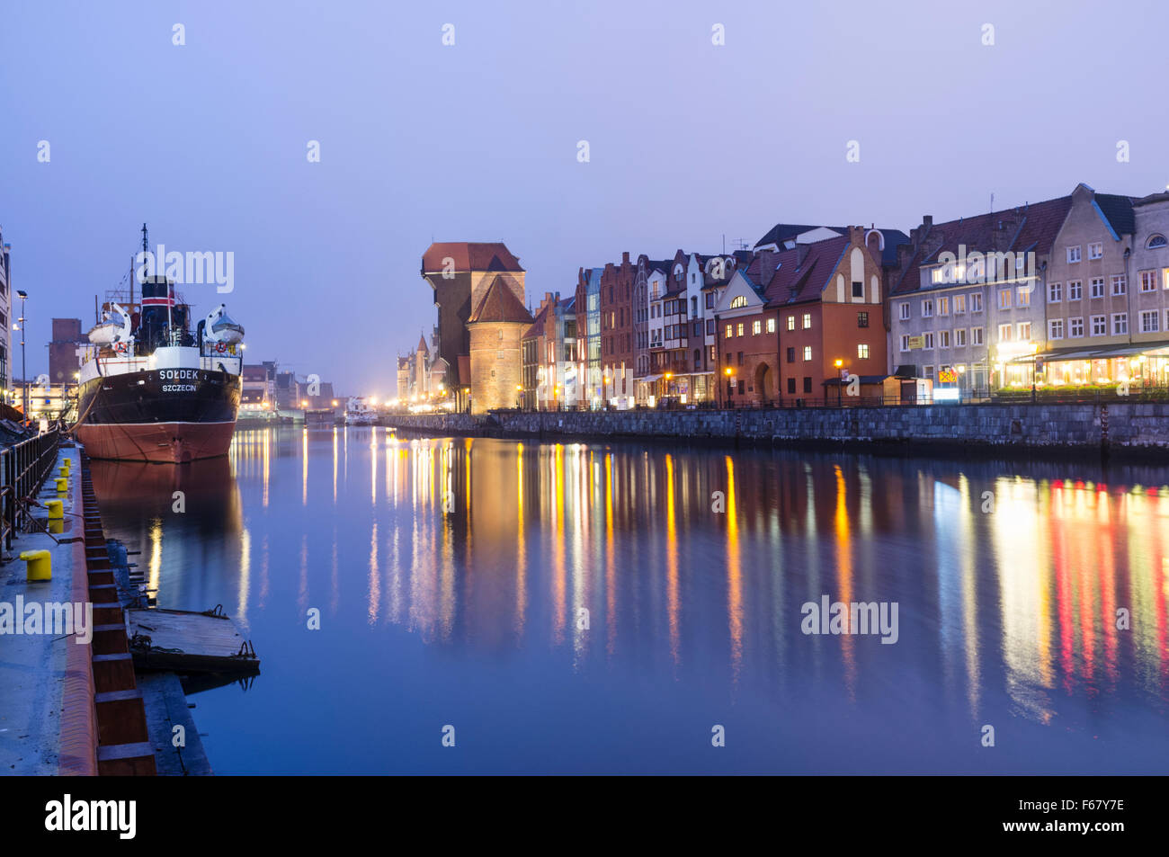 Waterfront tenements medieval crane and SS Sołdek museum ship reflected on Motlawa river at dusk. Gdansk, Poland. The SS Soldek Stock Photo