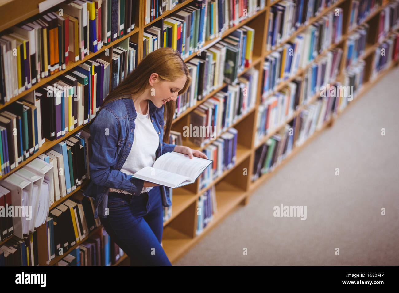 Student reading book in library leaning against bookshelves Stock Photo