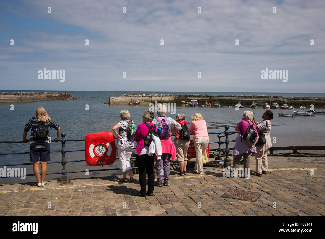 Rear view of group of mature female friends standing, looking over scenic harbour, Staithes, Yorkshire, England on sunny summer day with blue sky. Stock Photo
