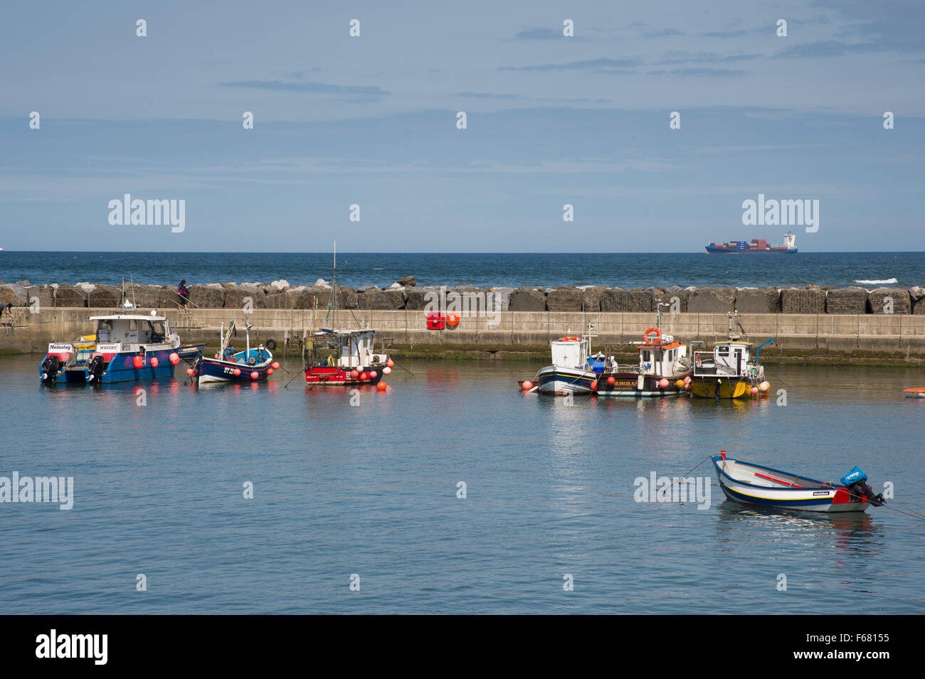 Fishing boats and cobles moored in the shelter of the scenic harbour, Staithes, North Yorkshire, UK on a calm, sunny summer day with blue sky & sea. Stock Photo