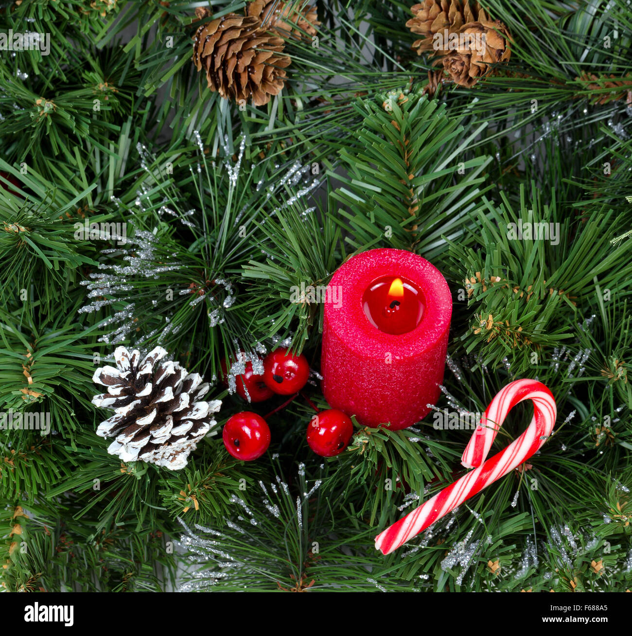 Glowing red candle and ornaments in evergreen setting. Stock Photo