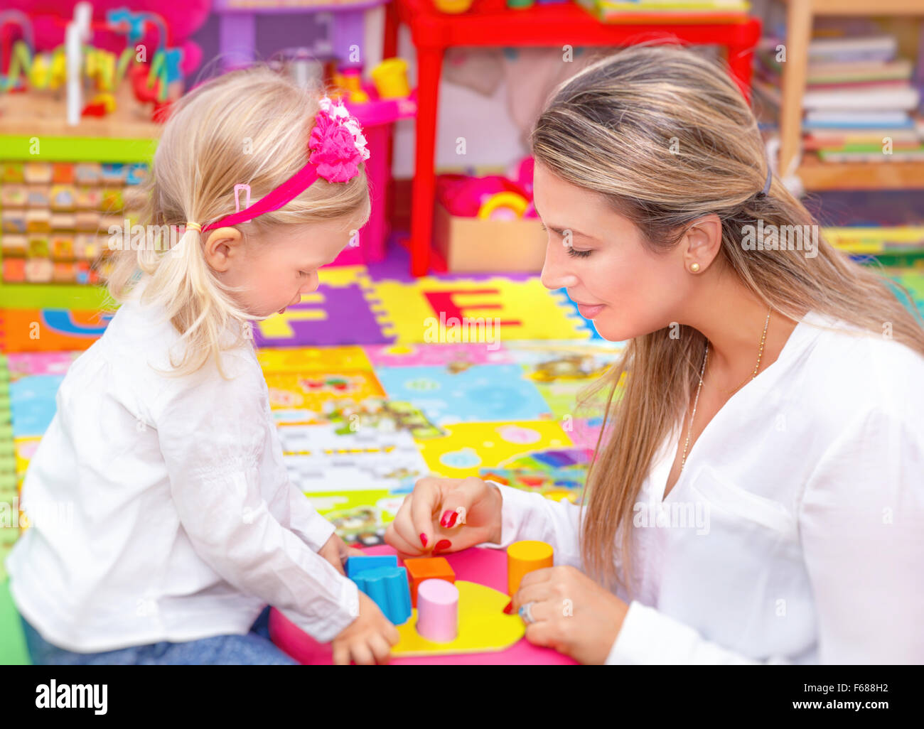 Cute little girl with young beautiful mother playing game in colorful playroom, happy family with pleasure spending time Stock Photo