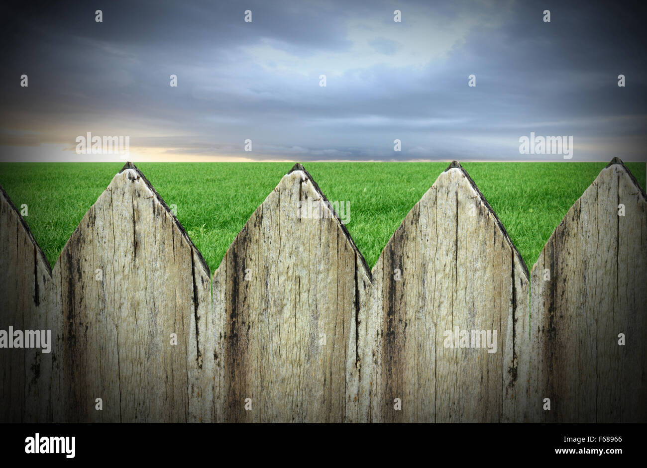 old picket fence in the foreground with lawn behind and grey sky Stock Photo