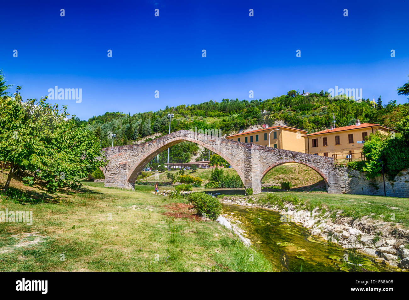 The XVIII century bridge in Modigliana in Italy is overlooking the quiet waters of the small creek with the medieval humpback structure of the three archs Stock Photo