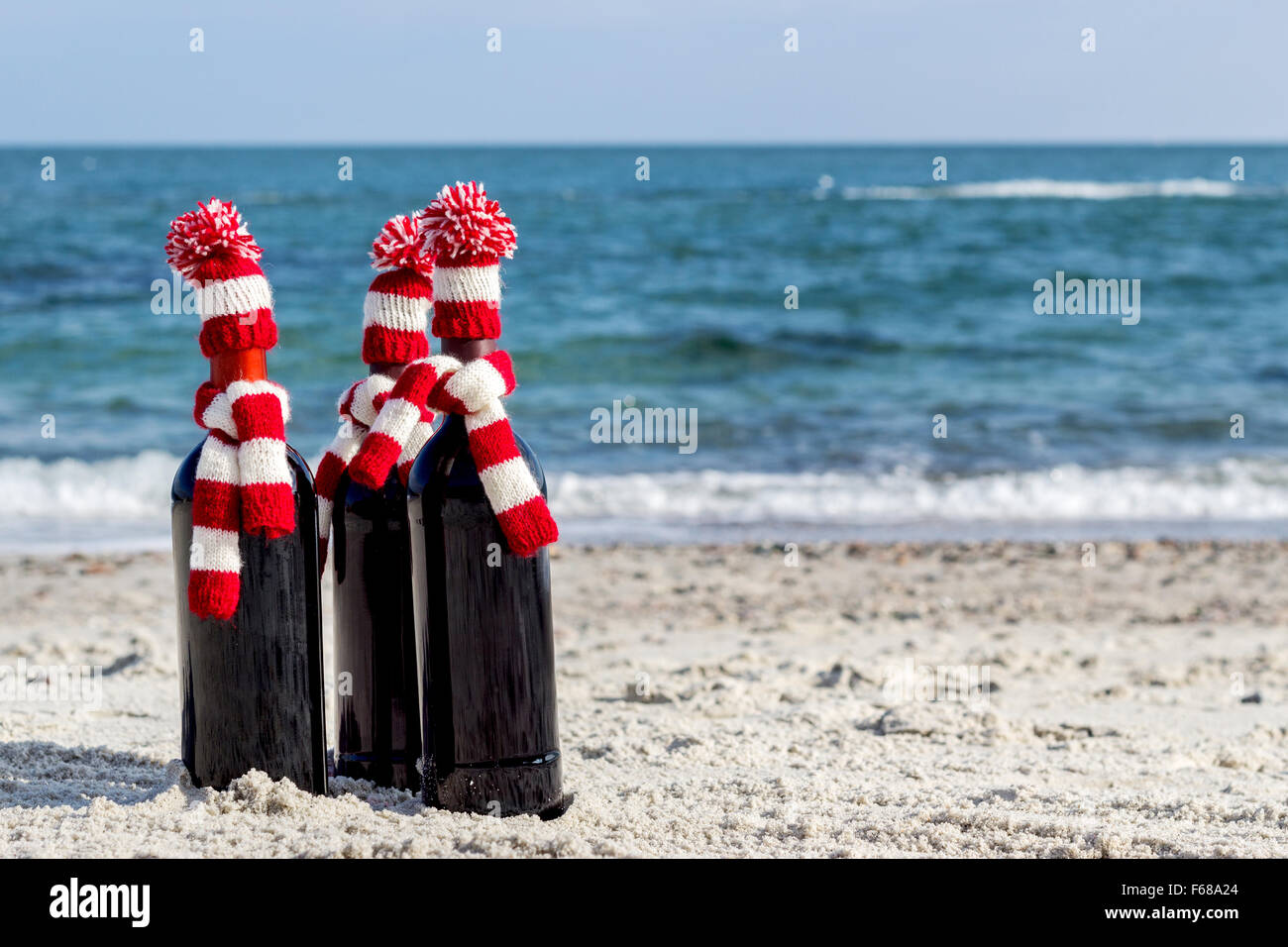 Christmas gifts. Three bottles of wine in knitted hats and scarves on the beach. Selective focus. Stock Photo