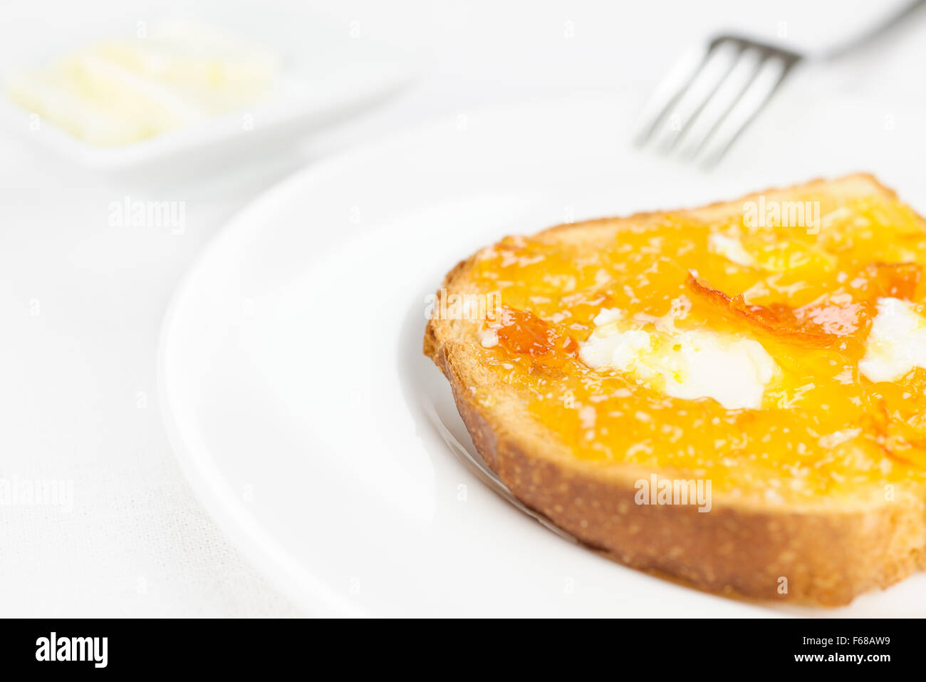 French toast with spread bitter orange marmalade or jam with candied peel, butter curls, fork on background and dishware on whit Stock Photo