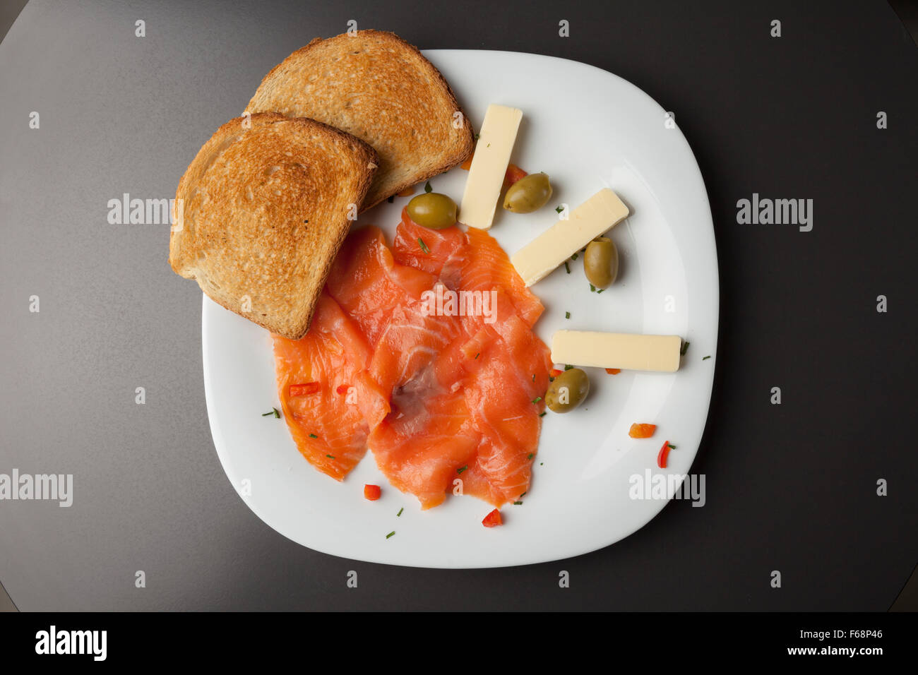 Smoked salmon filets with toasted bread and olives on white plate Stock Photo