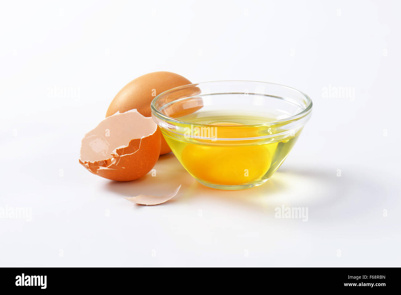 Fresh egg white and yolk in glass bowl, whole egg and eggshell Stock Photo
