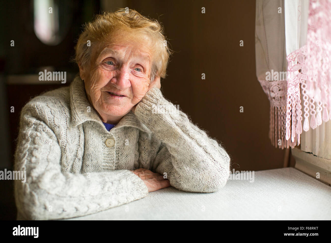 An elderly woman sitting dreamily by the window. Stock Photo