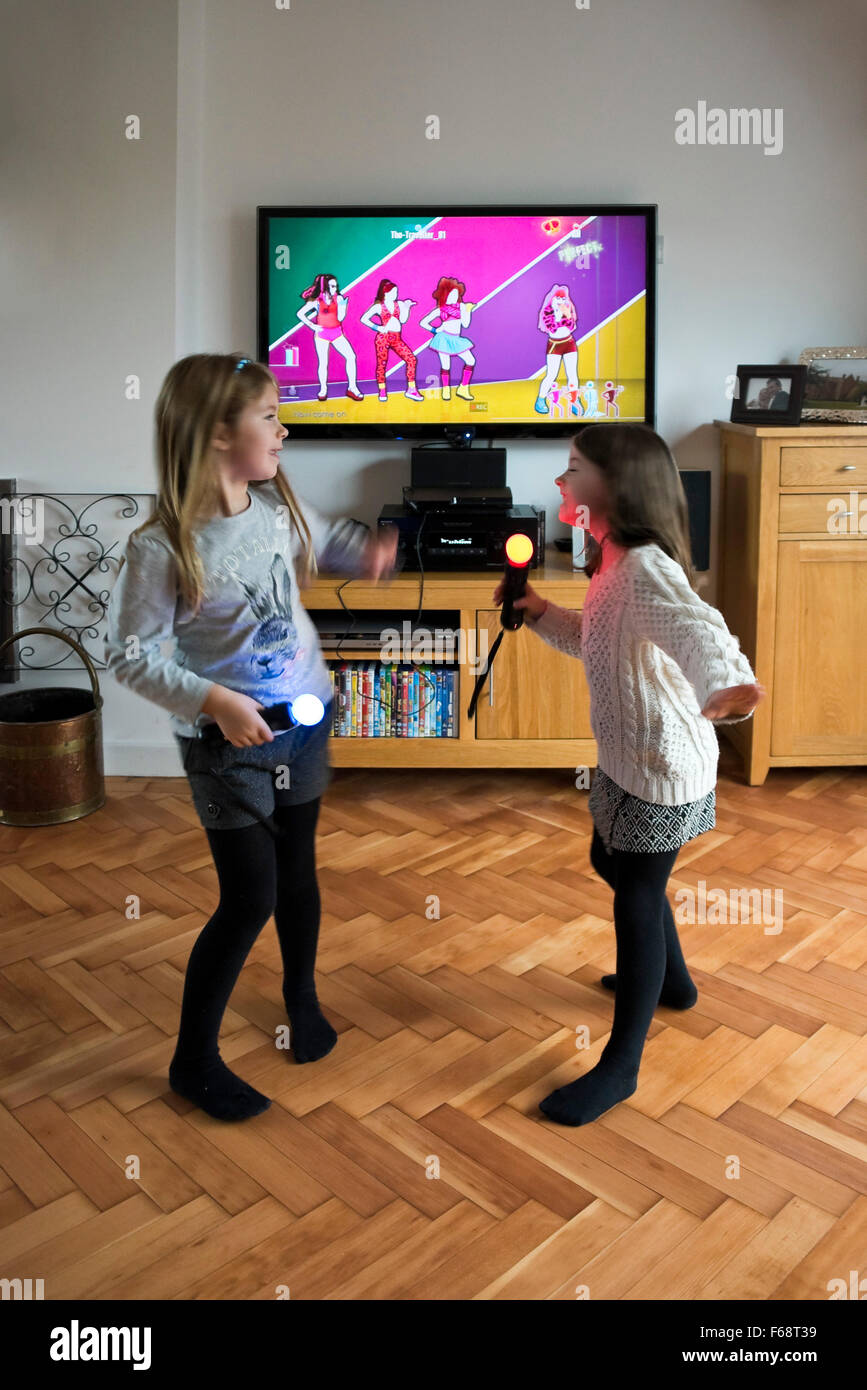 Vertical portrait of two little girls dancing and singing together on their games console. Stock Photo