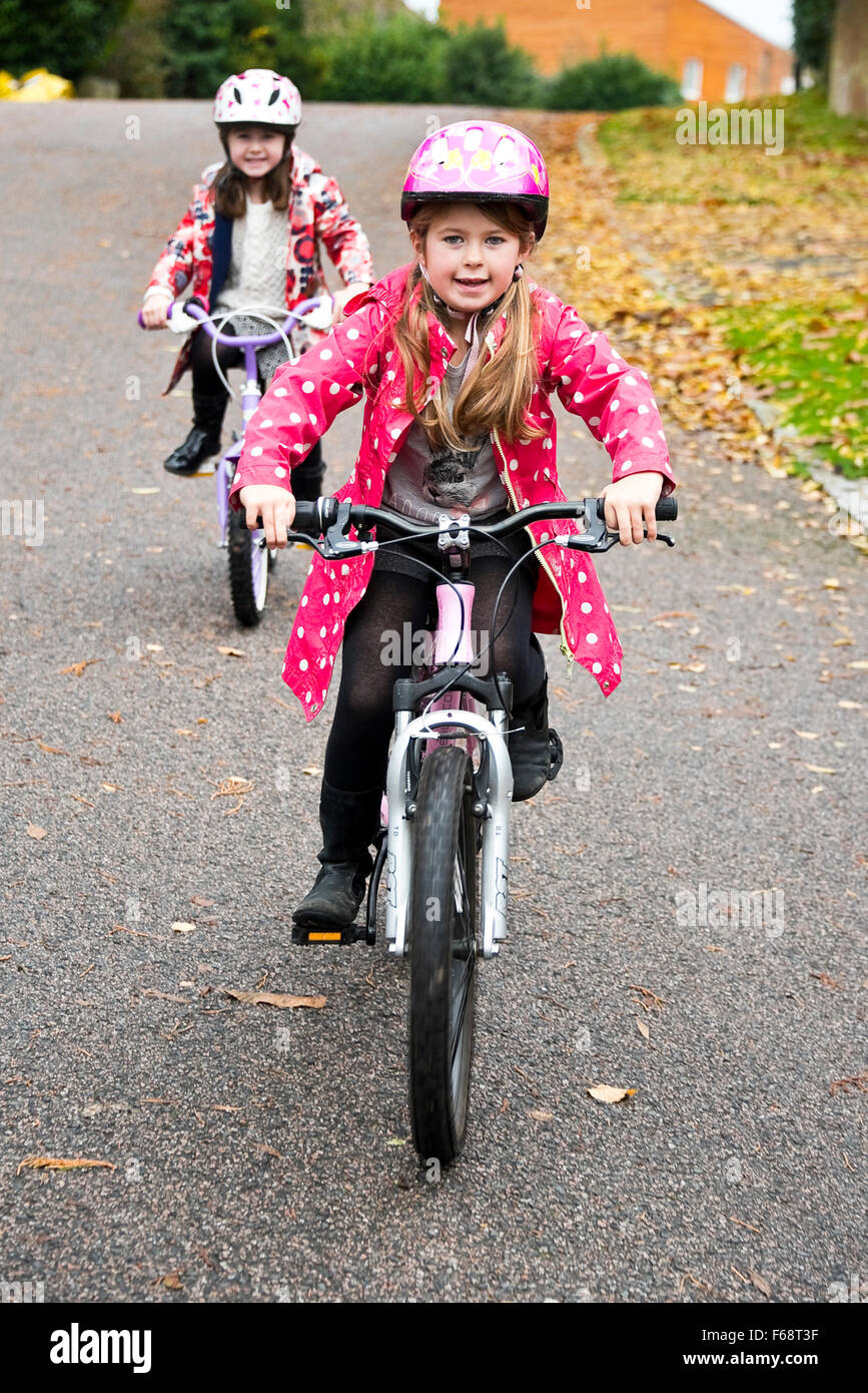Vertical portrait of two young girls riding their bikes on the road. Stock Photo