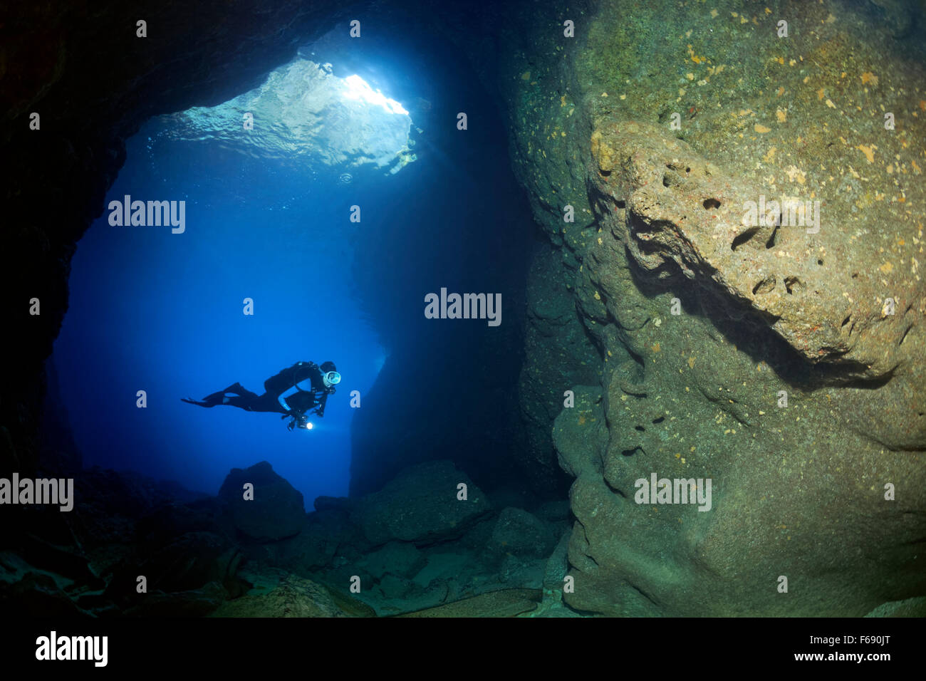 Diver with lamp in rocky cave, sparse growth, sponges (Polifera), Corfu, Ionian Islands, Mediterranean Sea, Greece Stock Photo