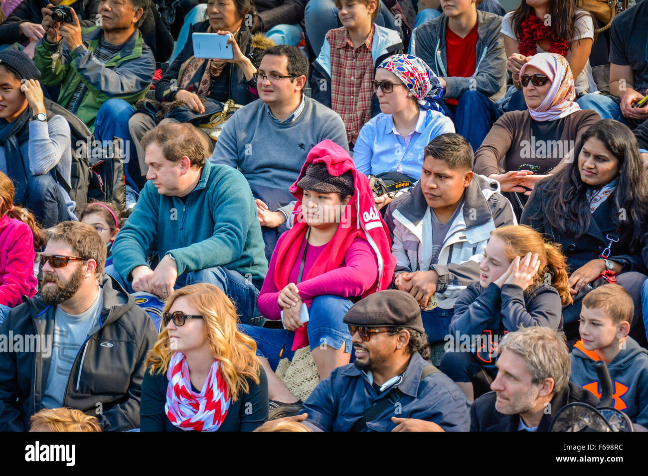 A large, diverse group of people sitting outside in rows as an audience watching a live performance and responding cheerfully Stock Photo