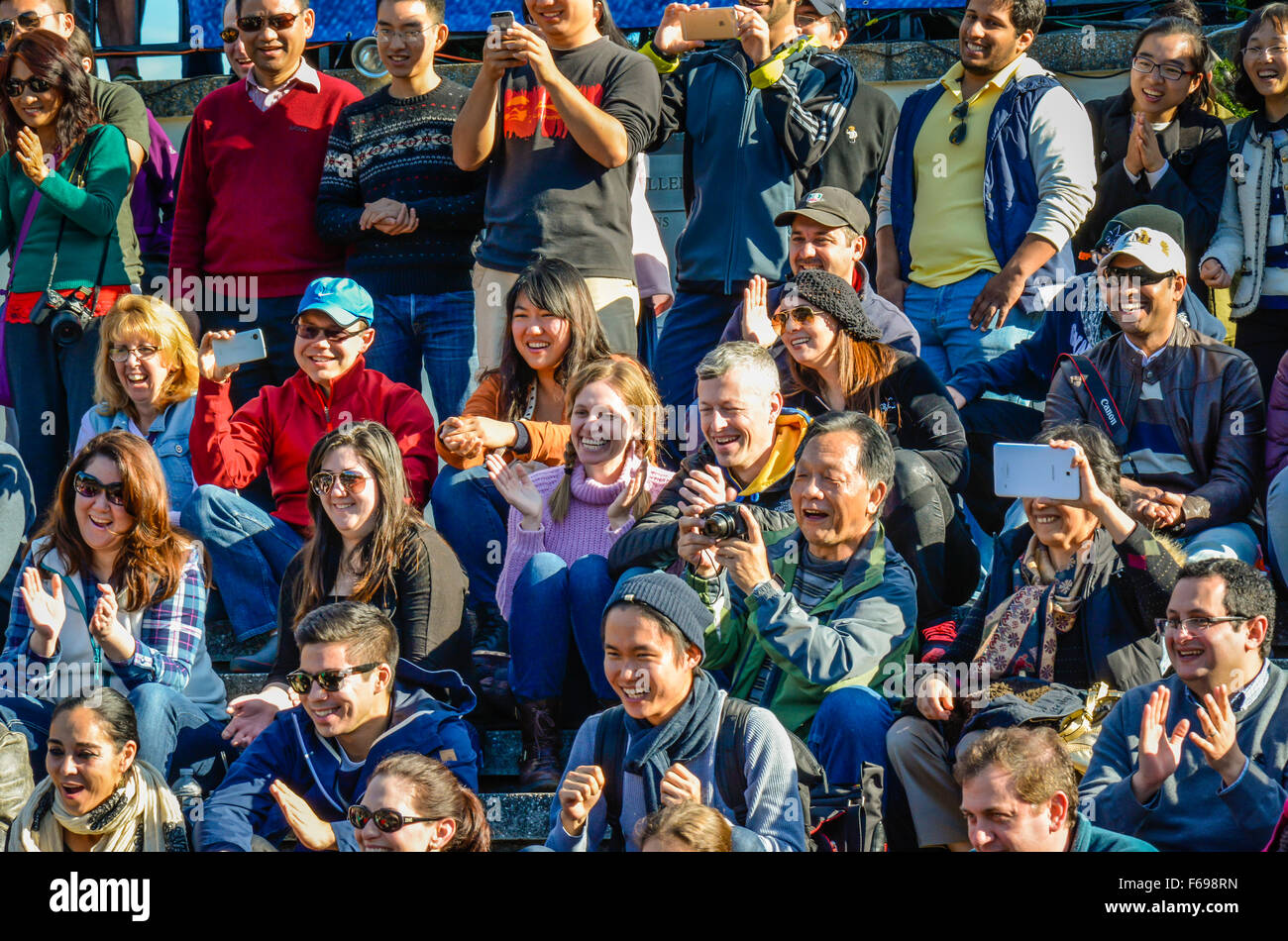 A large, diverse group of people sitting outside in rows as an audience watching a live performance and responding cheerfully Stock Photo