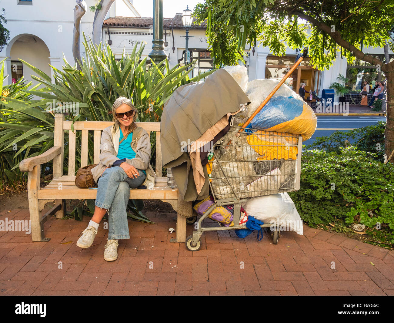 A senior citizen bag lady wearing sunglasses smiles ans sits on a public bench on State Street smoking a cigarette. Stock Photo