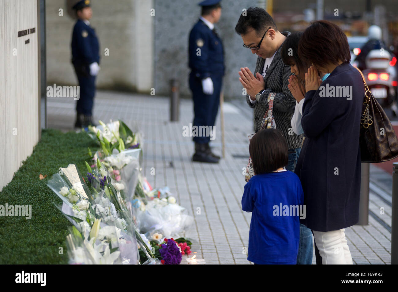 A Japanese family prays after laying flowers outside the French Embassy in Tokyo, following the terror attacks in Paris on November 13th. Stock Photo