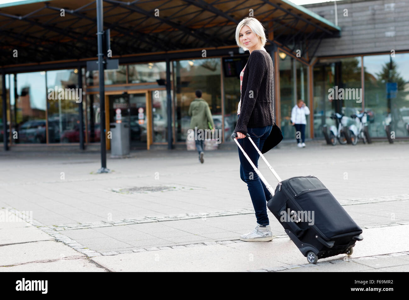 Smiling young woman traveling with a wheeled suitcase Stock Photo