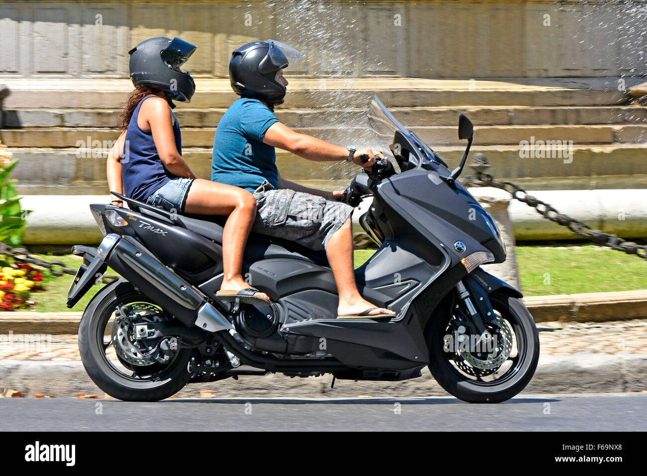 Young couple riding a Yamaha TMAX scooter passing a fountain in Aix en Provence South of France Stock Photo