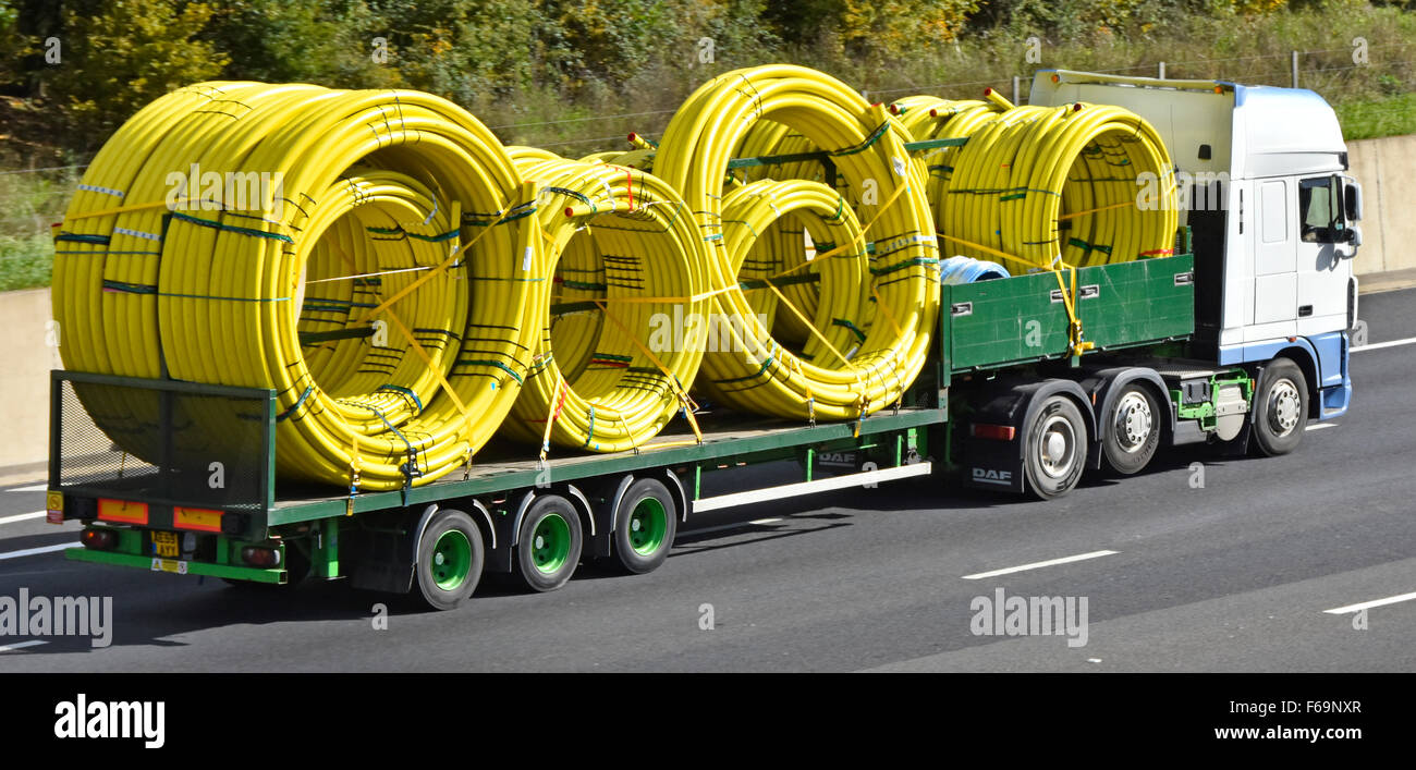 Side & back view lorry truck articulated trailer load of yellow coiled flexible plastic gas pipes various sizes driving on English UK M25 motorway Stock Photo