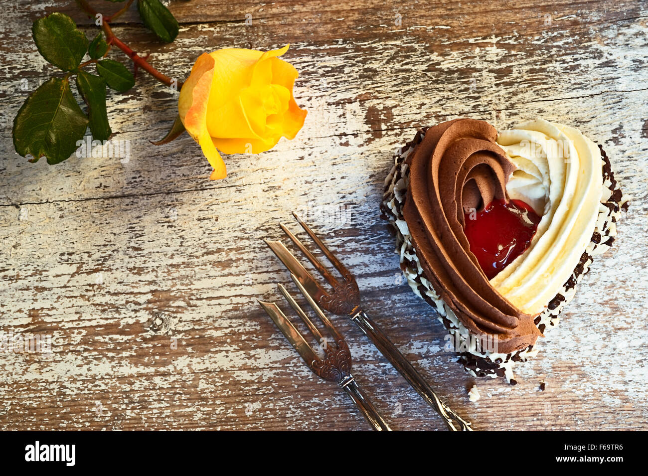 Still life with heart-shaped cake, two pastry forks and a yellow rose Stock Photo