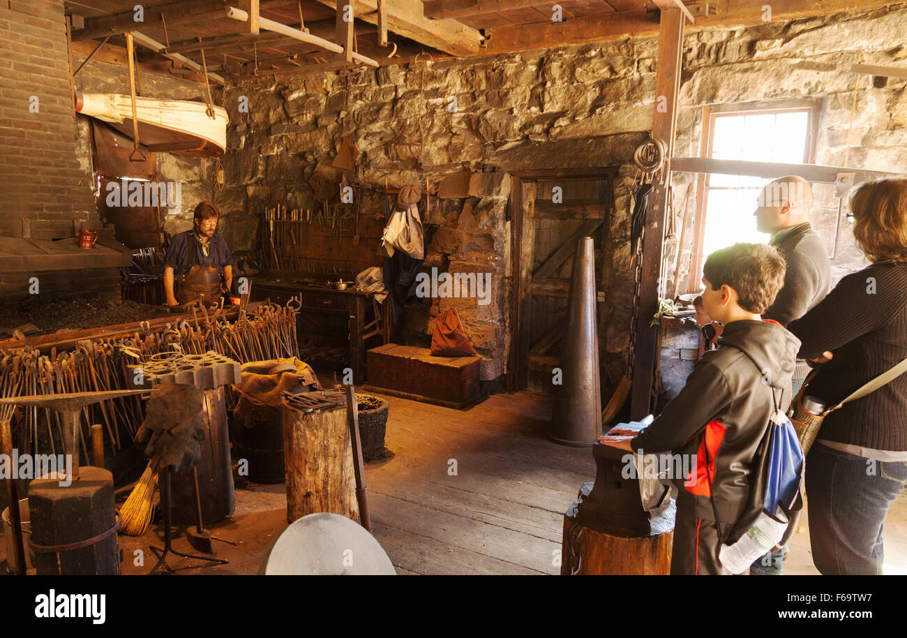 People watch an educational demonstration by a blacksmith in the 1800s, Old Sturbridge Village, Massachusetts MA USA Stock Photo